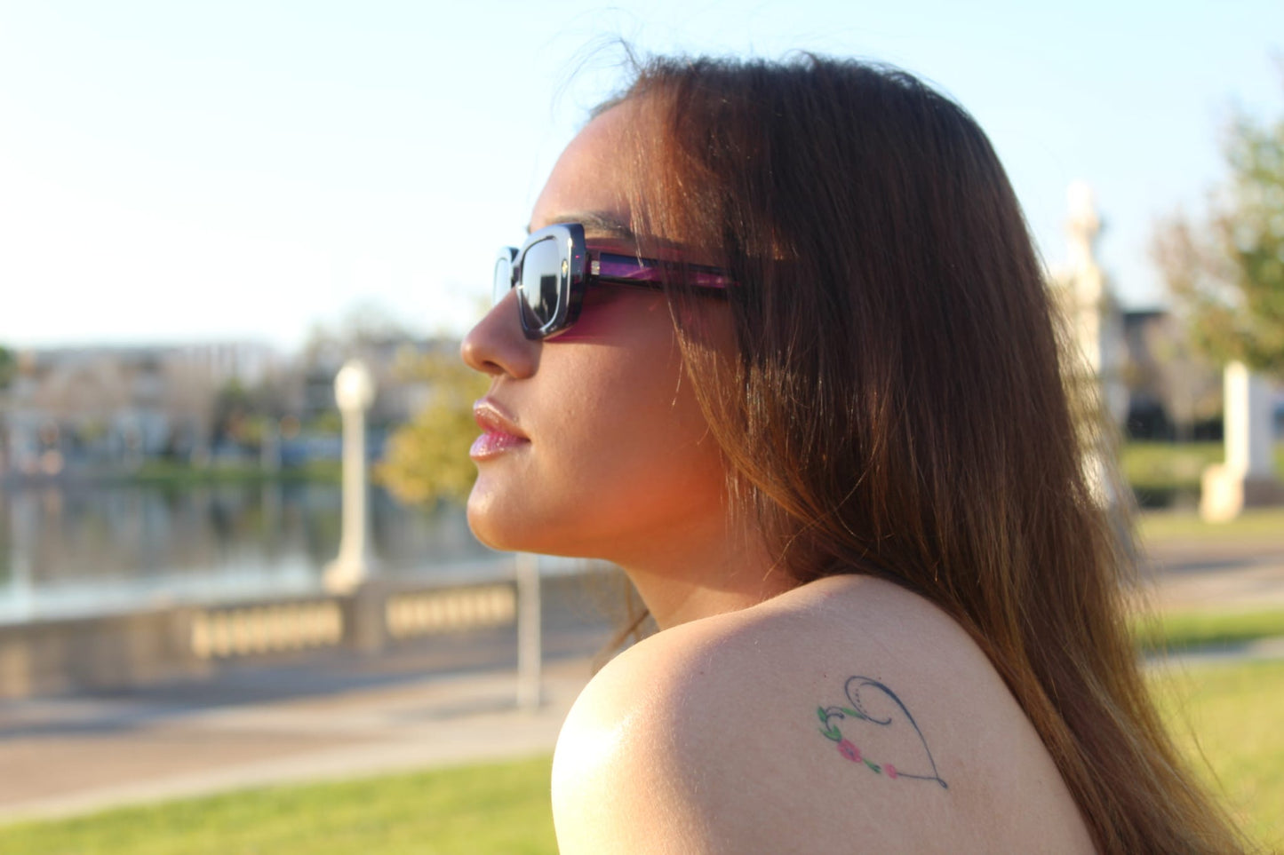 “Model wearing Cloud Jelly Gift sunglasses in glossy purple frame, facing sunlight with urban lake park in the background”
