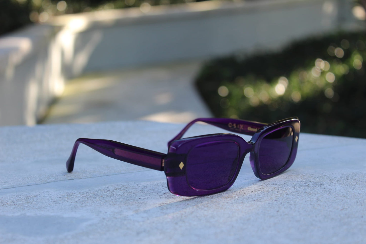 “Purple Gift sunglasses by Cloud Jelly resting on a white stone surface, capturing modern elegance in soft lighting”