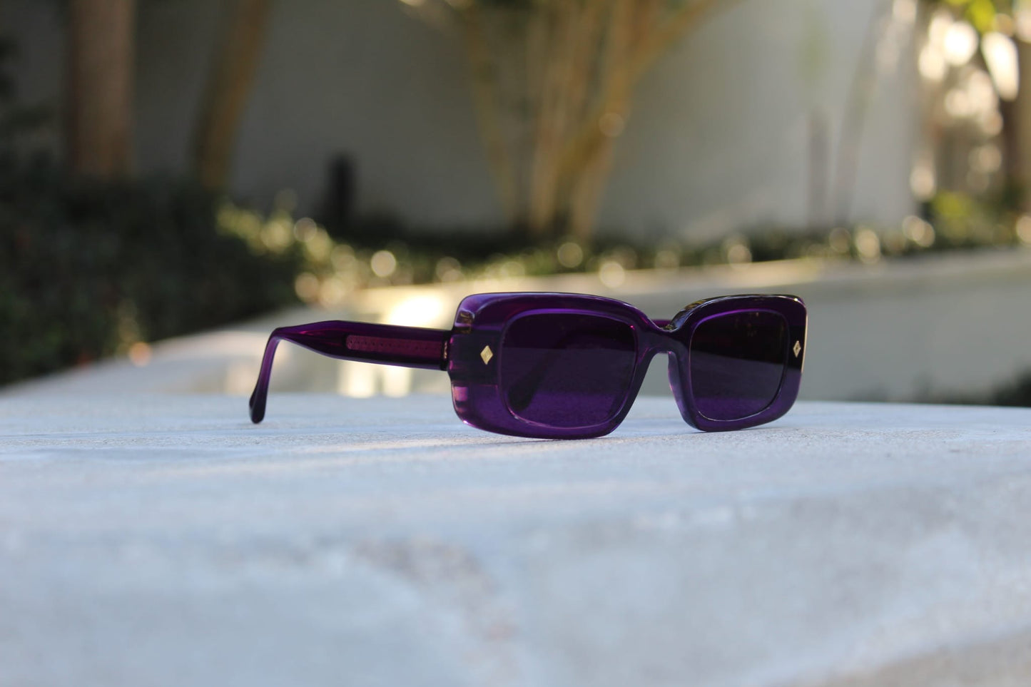 “Purple Gift sunglasses by Cloud Jelly resting on a white stone surface, capturing modern elegance in soft lighting”