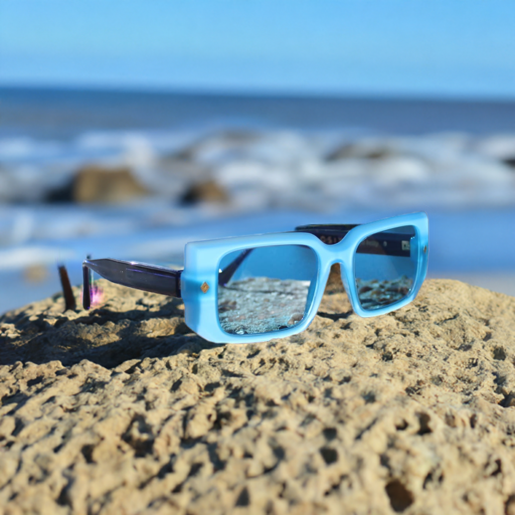 “Cloud Jelly River sunglasses resting on textured stone near water, featuring vibrant blue frame and urban background”