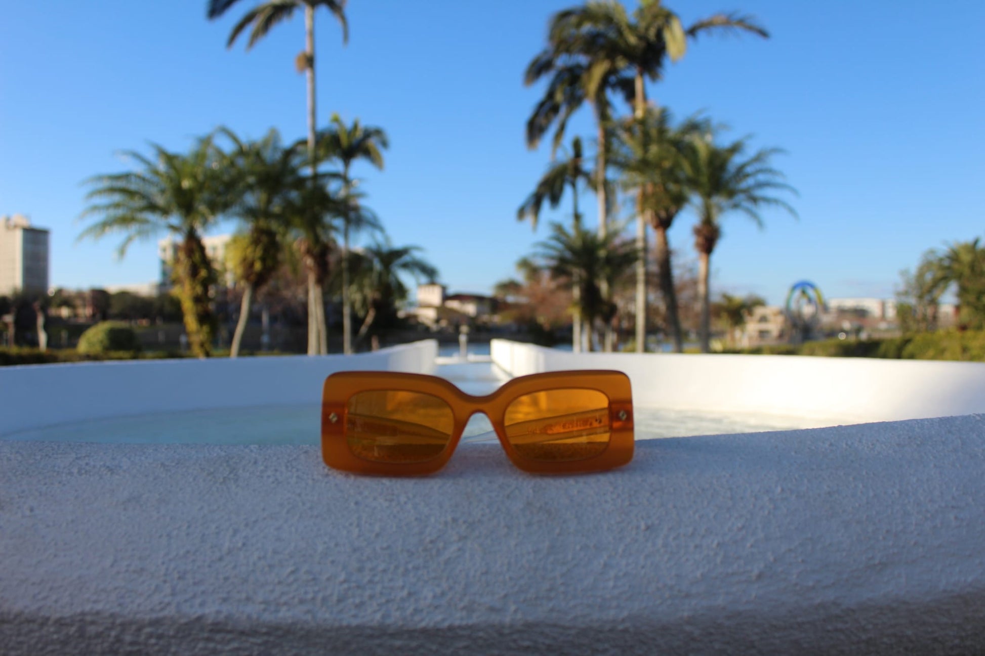 	“Sun sunglasses by Cloud Jelly on  tropical background, showcasing their trendy Orange design”